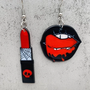 Detailed close-up of asymmetric Halloween acrylic earrings with lipstick and red lip motifs