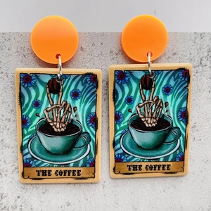 Detail of tarot card style earrings featuring a skull hand holding coffee beans on gray surface