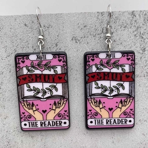 Detail of pink Tarot-style acrylic earrings featuring 'The Reader' book and hand motifs