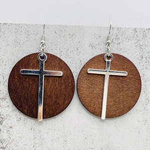 Detail of wooden drop earrings featuring a silver metal cross on a dark brown wood disc