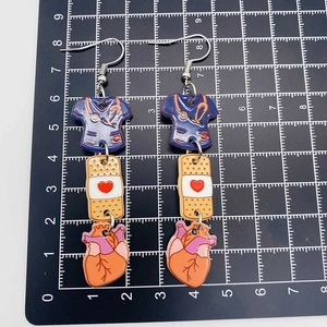 Detail of medical acrylic earrings featuring scrub top and anatomical heart charm