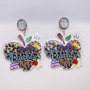 Gros plan des boucles d'oreilles pomme léopard avec texte Happy Teacher's Day et crayon
