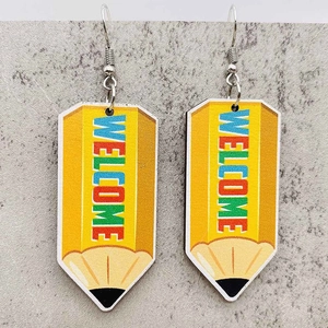 Close-up of yellow pencil drop earrings with Welcome text on marble background