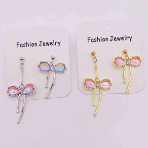 Détail de longues boucles d'oreilles avec nœuds roses irisés et pompons métalliques