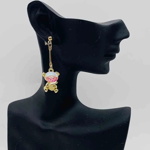 Détail de la boucle d'oreille pendante dorée avec un pendentif ours nacré rose et blanc