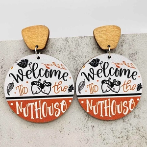 Detalle de pendientes de madera con estampado Welcome To the NUTHOUSE y motivos de otoño