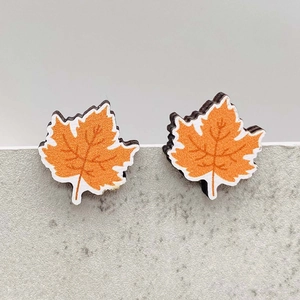 Macro detail of wooden maple leaf earrings with orange texture for Thanksgiving