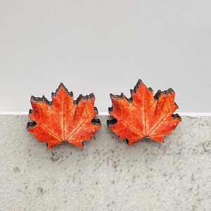 Close-up of wooden maple leaf earrings with realistic orange autumn texture and dark edges