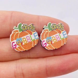 Macro detail of wooden pumpkin earring with Gobble text and leopard bow for Thanksgiving