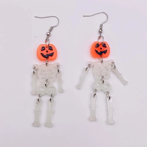 Close-up of Halloween drop earrings featuring orange pumpkin heads and glowing skeletons