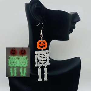 Glow-in-the-dark Halloween pumpkin and skeleton drop earrings on human model