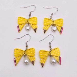 Detail of yellow pencil bow earrings with white heart and teardrop pearl charms