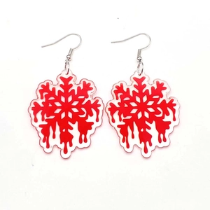 Detailed macro of red acrylic snowflake earrings with unique melting edges and silver hooks