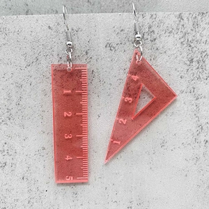 Orecchini creativi in acrilico rosso a forma di righello su sfondo in pietra grigia