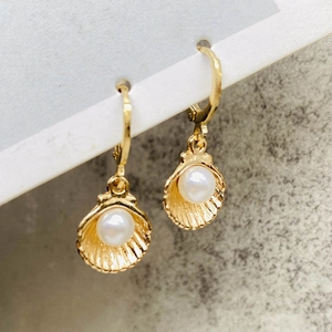 Boucles d'oreilles coquillage doré avec perle blanche sur surface en pierre