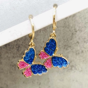 Macro view of butterfly earrings with dark blue and pink glitter in gold huggie hoops