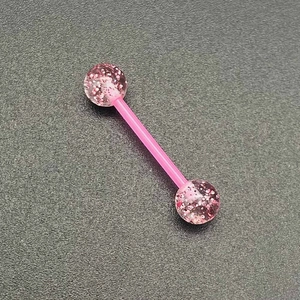 Gros plan d'un piercing en acrylique rose pailleté avec des billes brillantes sur fond gris