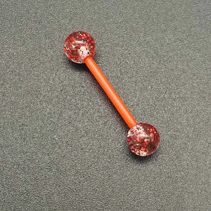 Détail d'un piercing barbell en acrylique orange avec des paillettes étincelantes à l'intérieur