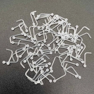 Close-up of bulk transparent L-shaped acrylic nose studs with ball ends on black background
