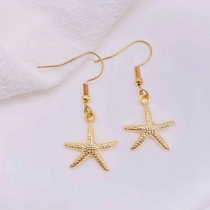Detail shot of golden starfish drop earrings with textured surface and hook findings