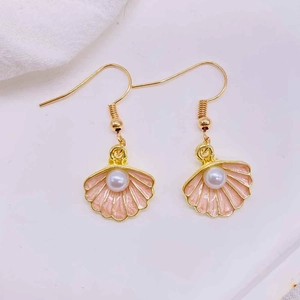 Detail of pink shell earrings with gold edges and a white pearl on white fabric