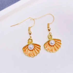 Macro detail of gold sea shell earrings with orange enamel and a white pearl center