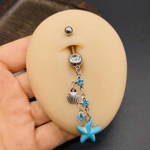 Dettaglio del piercing all'ombelico con pendenti a stella marina conchiglia e zirconi blu