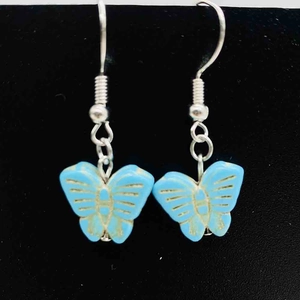 Détail de boucles d'oreilles papillon bleu ciel avec gravure dorée sur velours
