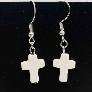 Détail de boucles d'oreilles bohèmes avec pendentif croix et crochets argentés sur fond noir