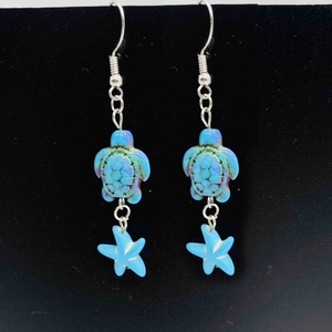 Détail des boucles d'oreilles pendantes tortue et étoile de mer et tortue bleu ciel et argent