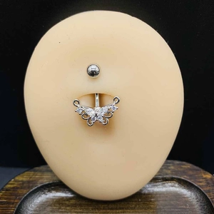 Détail d'un piercing de nombril papillon avec zircons blancs sur un modèle en silicone