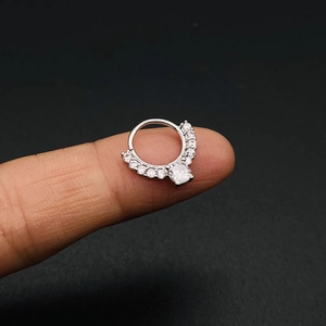 Detail van zilveren septumring met zirkonia stenen tussen de vingers voor maatreferentie