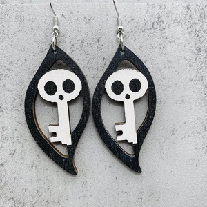 Detail of wooden leaf-shaped earrings featuring a white skull and key Halloween design