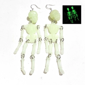 Detailed view of luminous skeleton earrings showing green glow in the dark effect