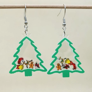 Macro shot of transparent acrylic Christmas tree earrings with festive miniature charms