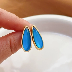 Elegant water drop earrings with dark blue gemstones and gold-plated frames on white tray