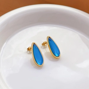 Detail of drop-shaped gold stud earrings with bright blue inlay on white ceramic plate