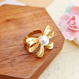 Detail of adjustable gold bow ring with white pearl on a wooden hexagonal display