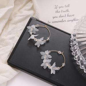 Detail of gold hoop earrings with matte white petals and clear beads on black stand