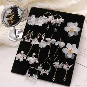 Elegant white petal drop earrings with gold tassels and pearls on a black display stand