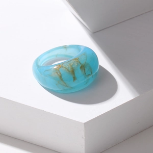 Close-up of translucent blue resin ring with golden marble texture on white stone