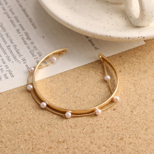 Detailed view of a gold open cuff bracelet featuring fine chains and elegant pearls