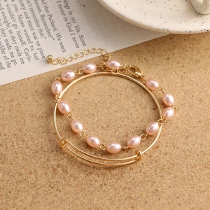 Detail of layered gold bracelet set with pink imitation pearls on a cork background