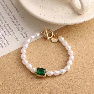Close-up of vintage pearl bracelet with emerald green gemstone and golden OT clasp detail