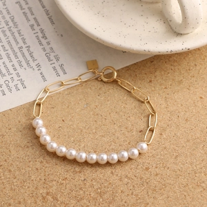 Close-up of mixed paperclip chain and white pearl bracelet with gold hardware