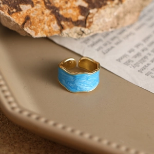 Detalle de anillo dorado ajustable con esmalte azul ondulado sobre papel vintage