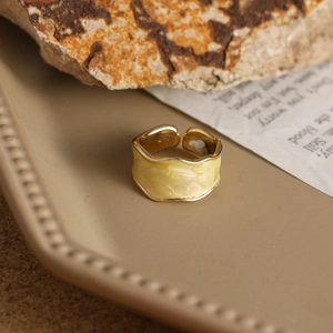 Detalle de un anillo dorado retro con textura de esmalte jaspeado crema sobre fondo piedra