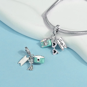 Detailansicht silberner Reise-Charms mit Kamera, rosa Sonnenbrille und Flugticket-Anhänger