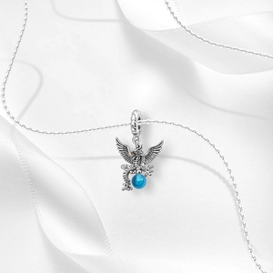 Macro detail of a silver dragon pendant holding a blue bead on a white silk background