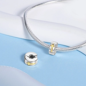 Macro shot of silver charm bead with golden cross relief on snake chain bracelet